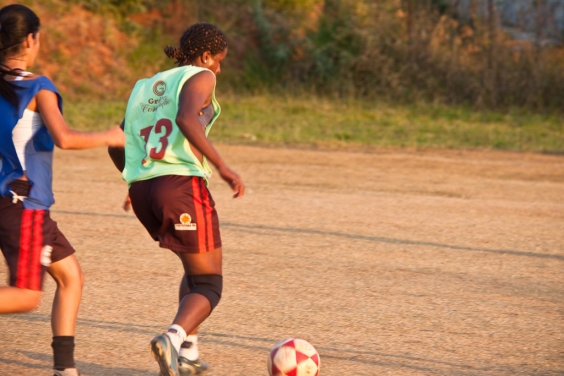 duas jogadoras em partida de futebol disputada em campo de terra