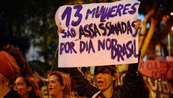 Mulheres fazem caminhada em solidariedade às manifestações feministas na América Latina, que tem países com alta taxa de feminicídio. Cartaz com os dizeres "13 mulheres são assassinadas por dia no Brasil"