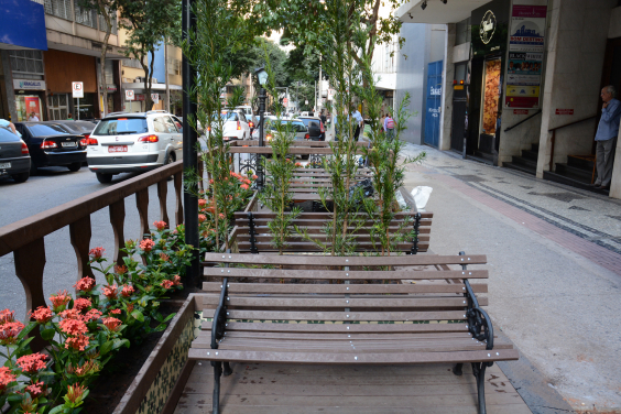 Calçada para pedestres e área de parklet com banco em madeira e flores