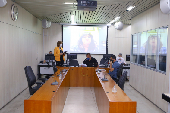 Vereadores compõem mesa de reunião. Telão ao fundo em videoconferência