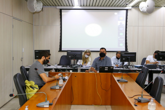 Vereadores compõem mesa de reunião no plenário Camil Caram. No telão, ao fundo, outros vereadores em videoconferência