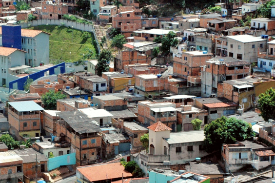 Foto do Aglomerado da Serra, durante o dia, com mais de 30 residências simples sobre área em declive.