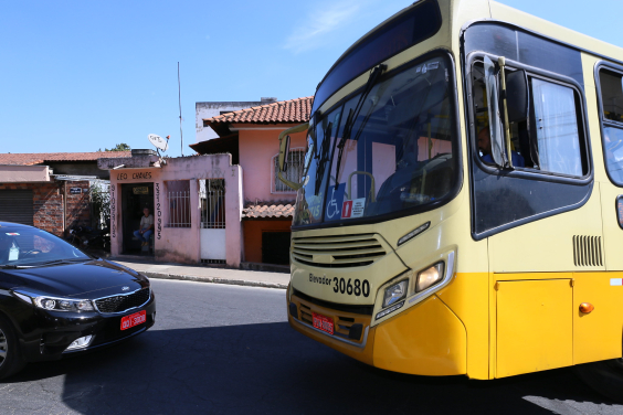Em uma via asfaltada, ônibus coletivo amarelo parado de frente para carro de passeio, na cor preta