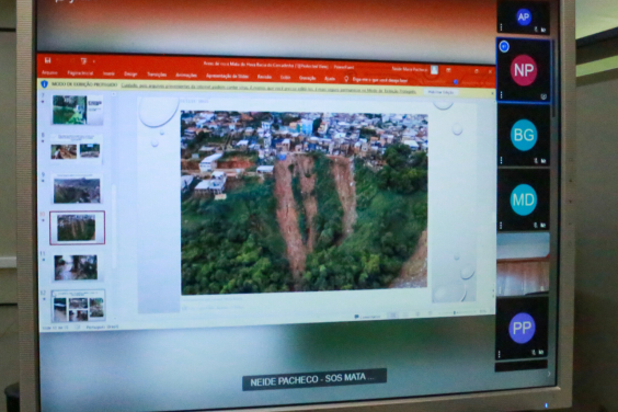 Tela de computador com imagem de encosta que ameaça deslizar. Alem de área verde ,  há também inúmeras casas  