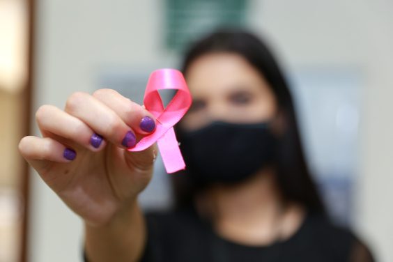 Mulher caucasiana segura laço de fita rosa - símbolo do combate ao câncer de mama. a mulher usa máscara e blusa na cor preta