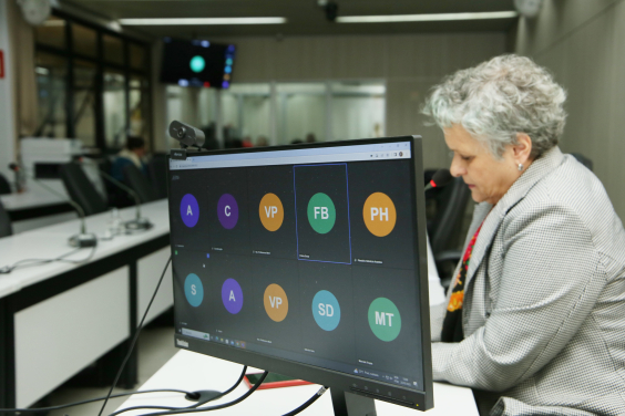 Imagem da tela do computador com indicação de participantes on line. ao fundo, a vereadora Cida Fallabela participa presencialmente 
