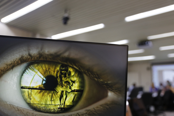 Imagem de uma menina de cabeça baixa diante de uma mão que simula um soco refletida na iris de um olho verde 