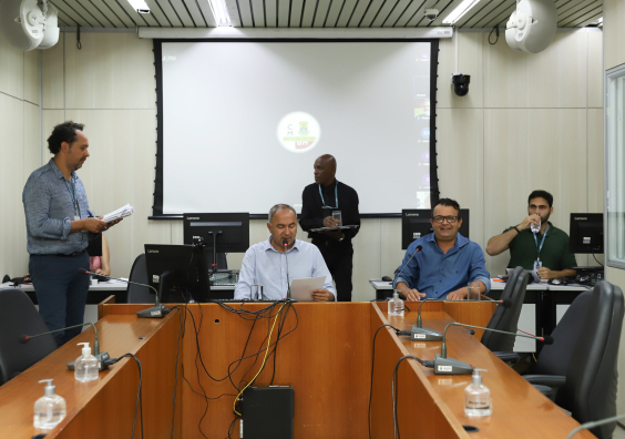 Dois vereadores participam de reunião, sentados à mesa.