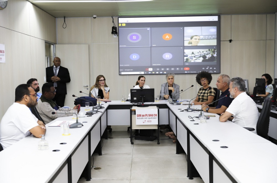 Foto de reunião conjunta. Vereadores estão sentados à mesa com um telão na parte de trás.