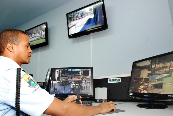 Telas mostram imagens de videomonitoramento da cidade; guarda municipal senta em frente ao computador