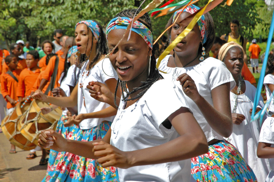 Três mulheres negras dançam vestidas de roupas tradicionais