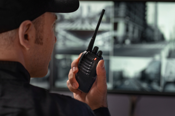 Vigilante aparece de lado, falando em walkie talkie