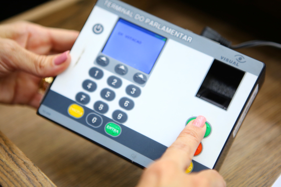 Mãos de parlamentar registrando voto em reunião plenária