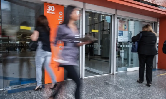fachada de agência bancária, com pessoas entrando e saindo do estabelecimento