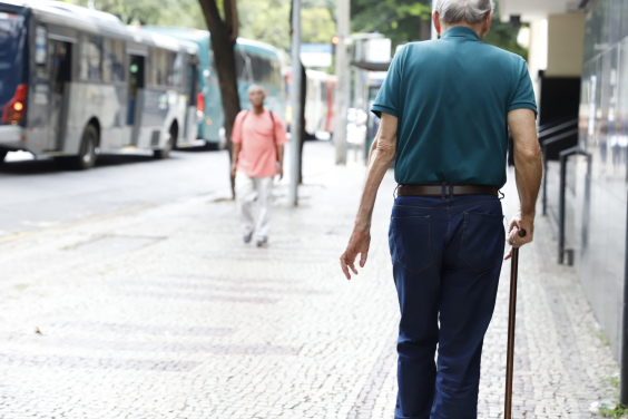 Idoso andando na calçada com auxílio de bengala