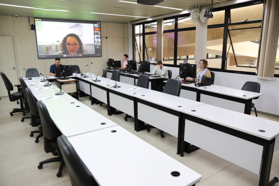 Vereador no Plenário Helvécio Arantes, com convidado aparecendo no telão ao fundo