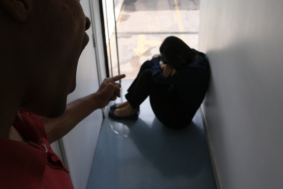 homem de pé aponta para mulher sentada no chão em cena de violência