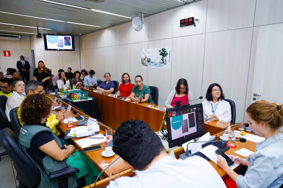 Vereadora Luiza Dulci e convidados em torno da Mesa do Plenário Camil Caram e ao fundo, pessoas acompanham da plateia.