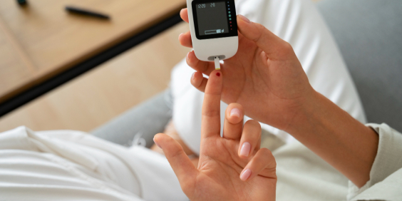 Vista superior de mulher com diabetes verificando seu nível de glicose em um aparelho medidor; ela tem o dedo furado com uma gota de sangue