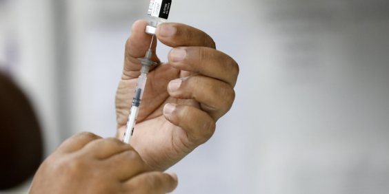 Duas mãos segurando uma seringa e ampola com vacina