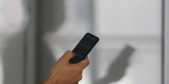 Mão segura celular com sombra de pessoa aparecendo ao fundo