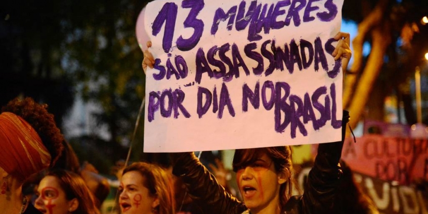 Mulheres fazem caminhada em solidariedade às manifestações feministas na América Latina, que tem países com alta taxa de feminicídio. Cartaz com os dizeres "13 mulheres são assassinadas por dia no Brasil"