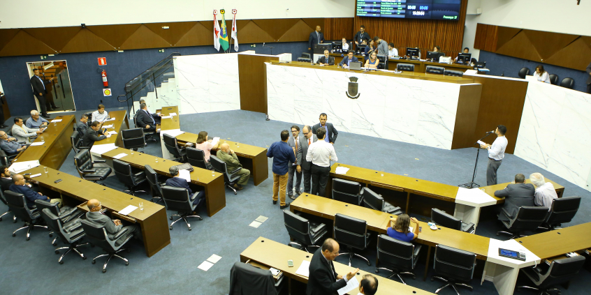 Vereadores sentados no Plenário, diante da Mesa Diretora; um parlamentar está de pé ao microfone