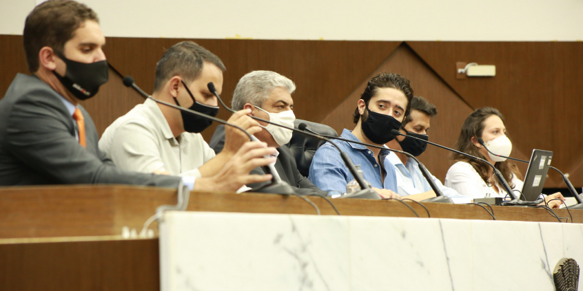 Cinco vereadores e uma vereadora sentados à mesa, portanto máscaras no rosto.