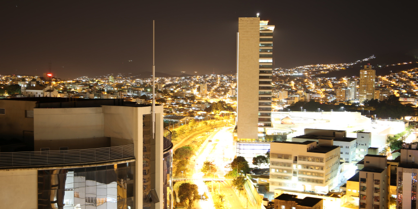 Fotografia noturna, vista panorâmica da cidade. Rio Arrudas ao centro, prédios iluminados.