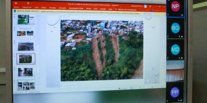 Tela de computador com imagem de encosta que ameaça deslizar. Alem de área verde ,  há também inúmeras casas  