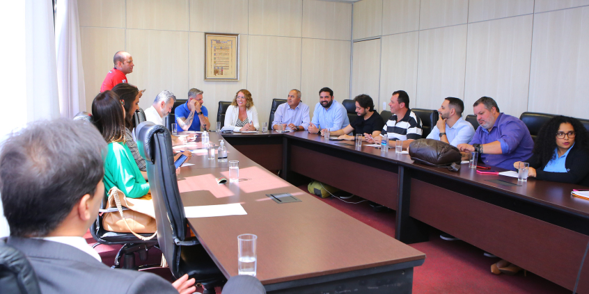 Imagem dos participantes da reunião sentados em uma mesa em formato de U. Na cabeceira da mesa, a presidente Nely Aquino 