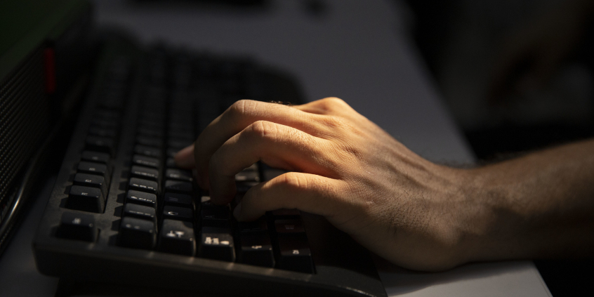 Imagem da mão de um homem caucasiano trabalhando no teclado de um computador