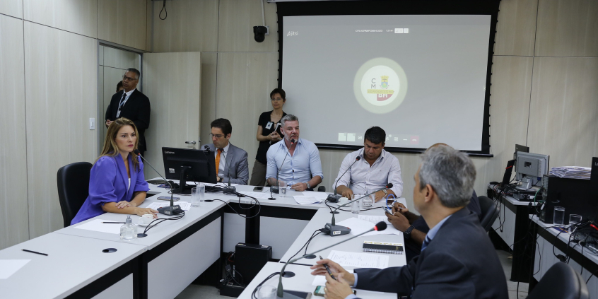 Seis parlamentares em reunião, sentados à mesa, acompanhados por dois assessores da Câmara, de pé, ao fundo