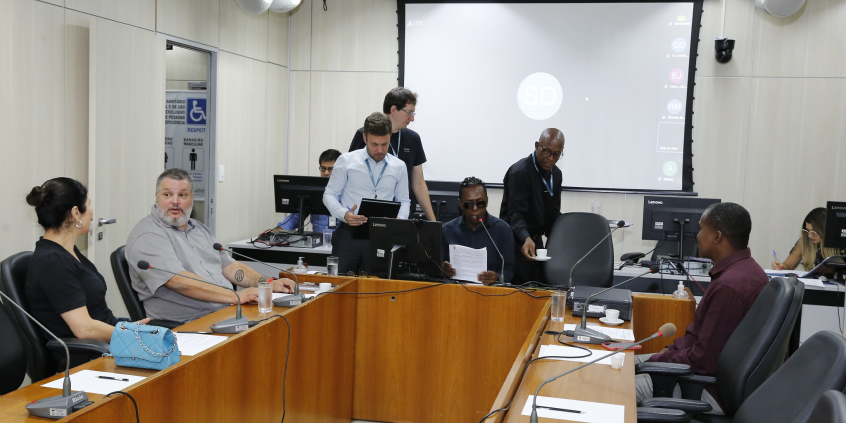 Imagem de vereadores que participam de reunião sentados em uma mesa em U