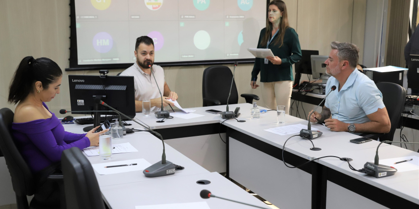 Três vereadores participam de reunião, sentados à mesa.