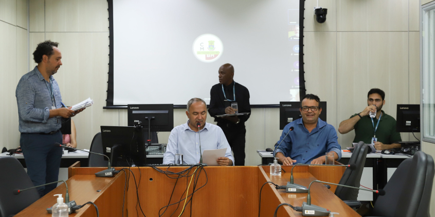 Dois vereadores participam de reunião, sentados à mesa.