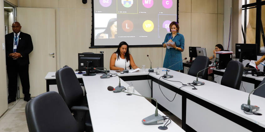 Sentada à mesa, vereadora realiza reunião virtual com outras duas parlamentares.