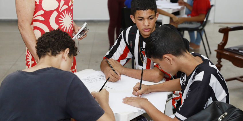 Três estudantes desenhando, sentados à mesa.