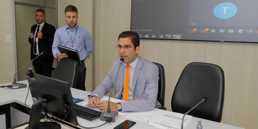 Parlamentar sentado à mesa, participando de reunião virtual com outros vereadores.