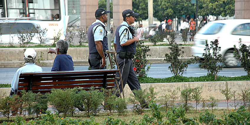 Dois guardas civis municipais caminham em uma praça, durante o dia