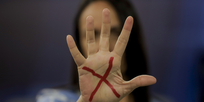 mulher branca com braço esticado na frente do rosto com a mão em sinal de pare