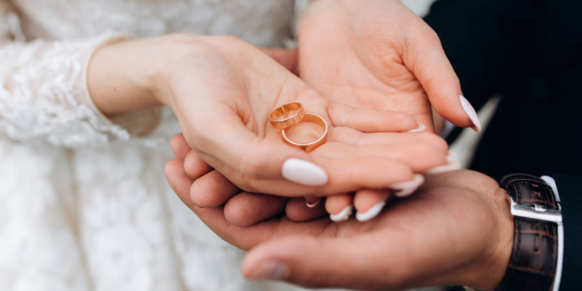 noivo segura as mãos de noiva onde estão dois anéis de casamento