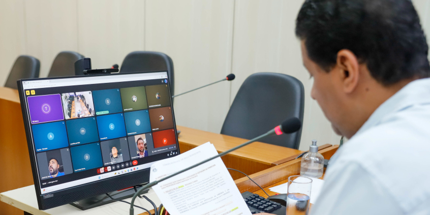 Vereador presidente da reunião conjunta em frente a tela com demais vereadores para apreciar parecer