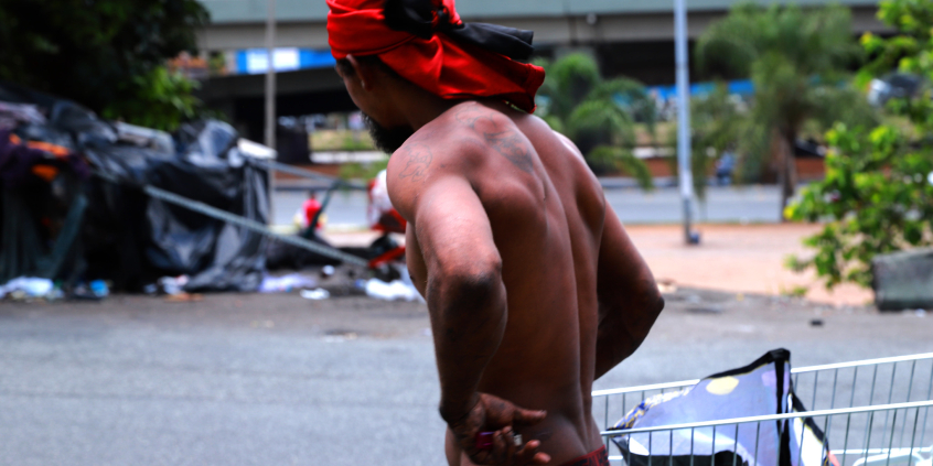 homem sem camisa visto de costas ao lado de um carrinho de supermercado