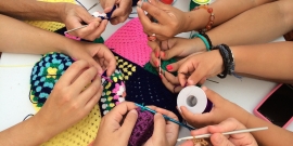 Várias mãos trabalhando juntas na confecção de um peça de crochê