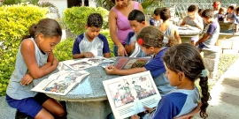 Crianças lendo livros infantis ao ar livre, acompanhados da professora