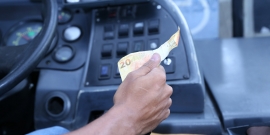 Motoristas segura o volante e uma nota de 20 reais
