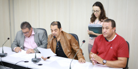 Três vereadores integrantes da comissão sentados à Mesa do Plenário Camil Caram apreciam a pauta da reunião