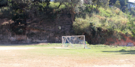 campo de futebol de várzea abandonado, em terra batida. Trave do gol ao centro com rede destruída