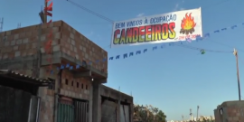 Imagem mostra algumas moradias populares e uma faixa escrito "Bem vindos à Ocupação Candeeiro"